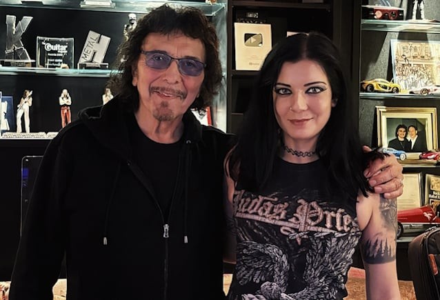 Tony Iommi i Becky Baldwin, drets i abraçats, en una sala amb vitrines de premis i discos d'or al fons