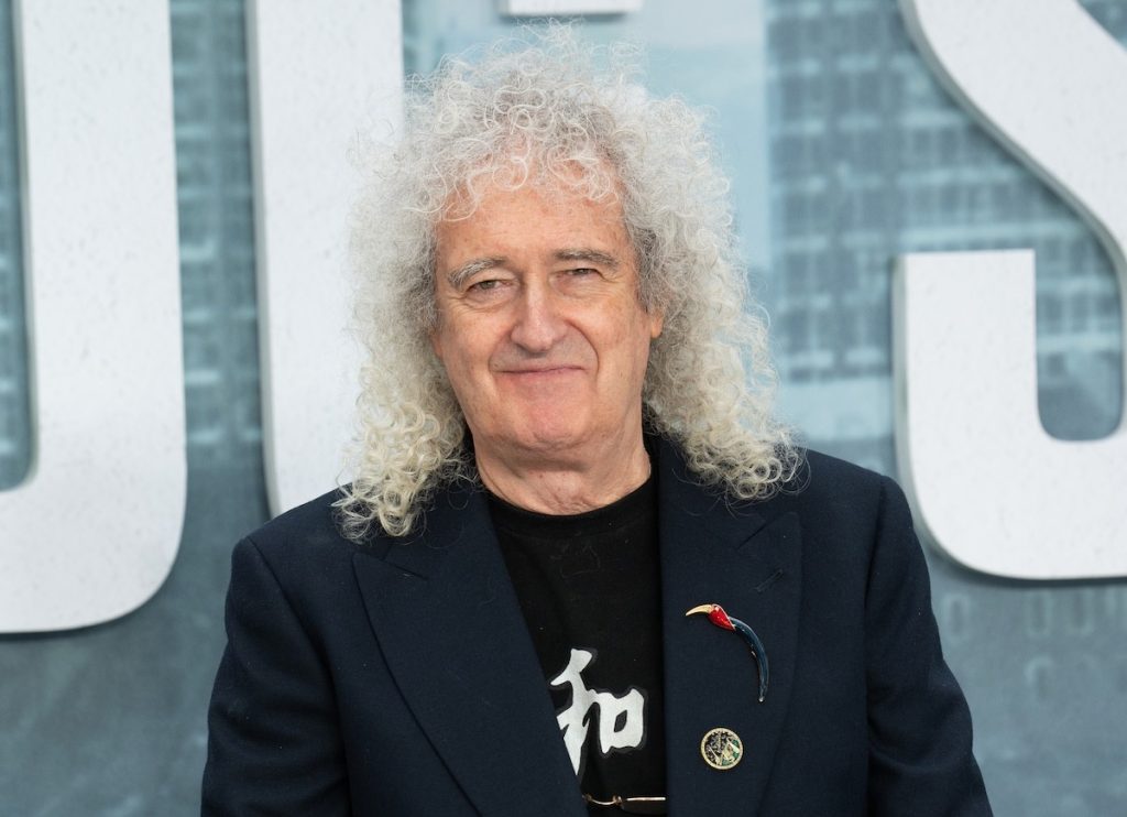 Brian May tocant la guitarra en un concert de Queen, amb la mà dreta alçada sobre les cordes