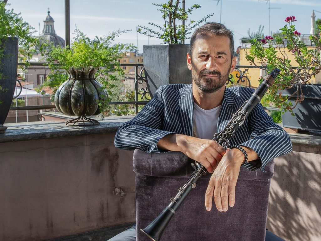 Francesco Bearzatti, assegut en una terrassa amb plantes i una cúpula al fons, recolza els braços al respatller d'una butaca amb un clarinet a les mans