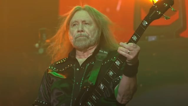 Ian Hill tocant el baix en un concert de Judas Priest, amb la llum vermella i verda de l'escenari al darrere