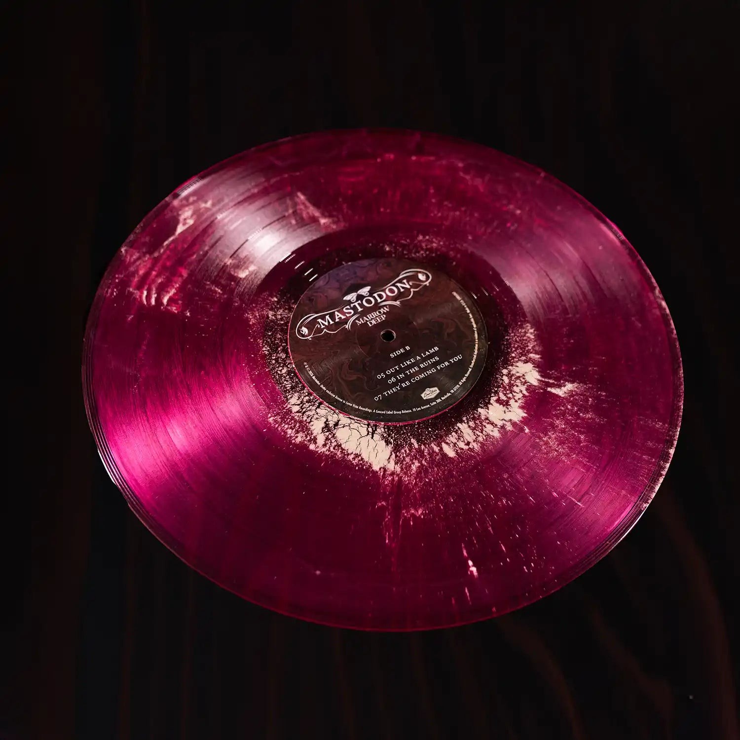 Cara B del vinil magenta de «Marrow Deep» de Mastodon, amb els grumolls blancs de pols d'os fòssil repartits pel solc