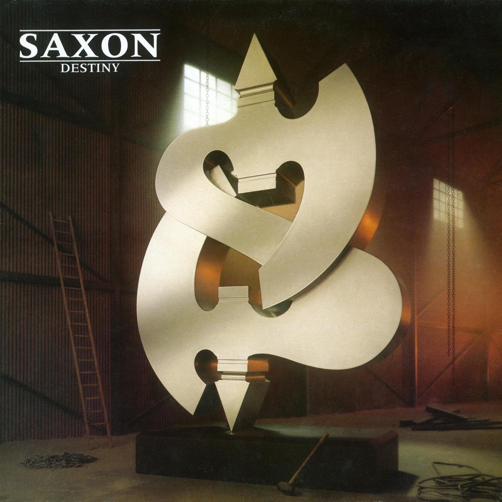 Portada de «Destiny», de Saxon: una escultura metàl·lica platejada en forma de doble essa, rematada amb dues puntes de fletxa, dins d'una nau industrial amb una escala de fusta i una maça a terra