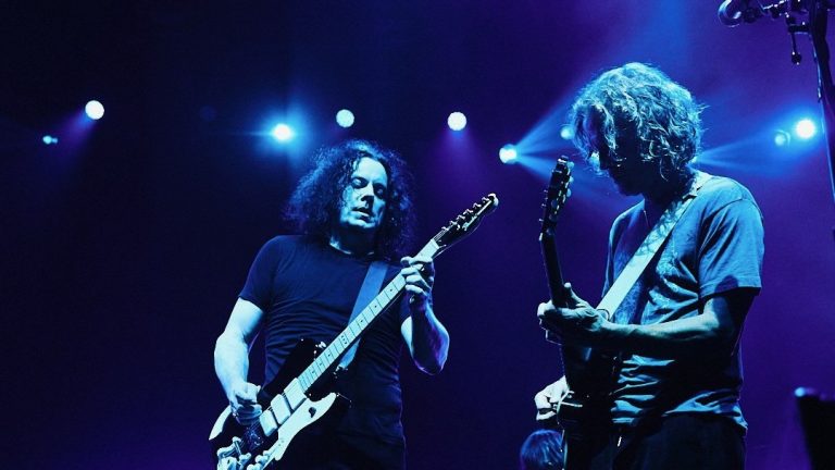 Jack White i Brendan Benson, els dos amb guitarra, il·luminats de blau damunt d'un escenari en un concert dels Raconteurs